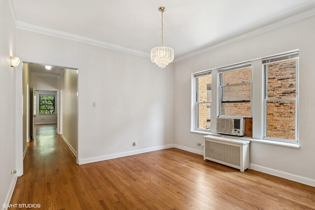 empty room featuring ornamental molding, wood finished floors, baseboards, radiator heating unit, and a notable chandelier