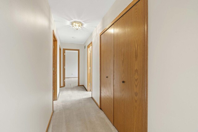 hall featuring baseboards and light colored carpet