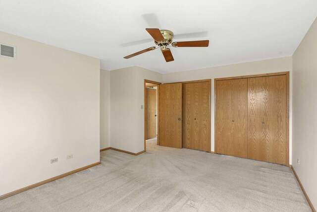 unfurnished bedroom with a ceiling fan, visible vents, baseboards, two closets, and light carpet