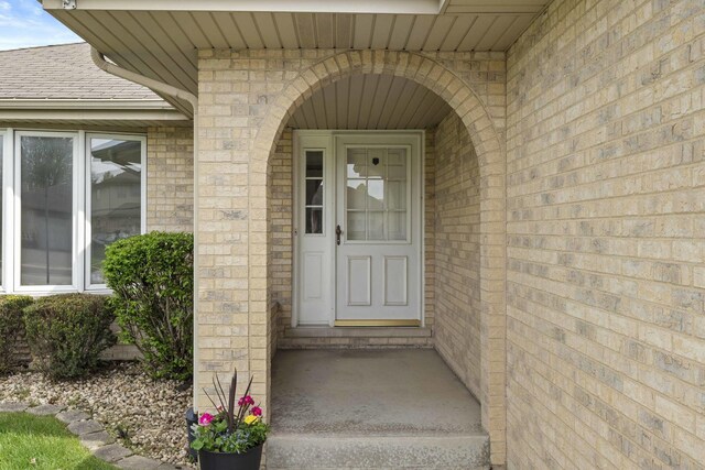 doorway to property featuring brick siding and roof with shingles