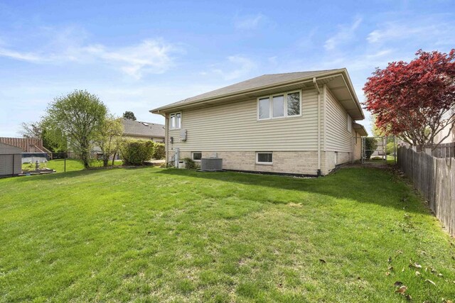 rear view of property featuring a fenced backyard, central AC, and a yard