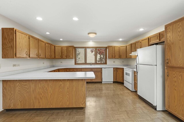 kitchen featuring light countertops, a sink, a peninsula, under cabinet range hood, and white appliances