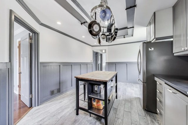 kitchen featuring wainscoting, light wood-style floors, crown molding, dark countertops, and freestanding refrigerator