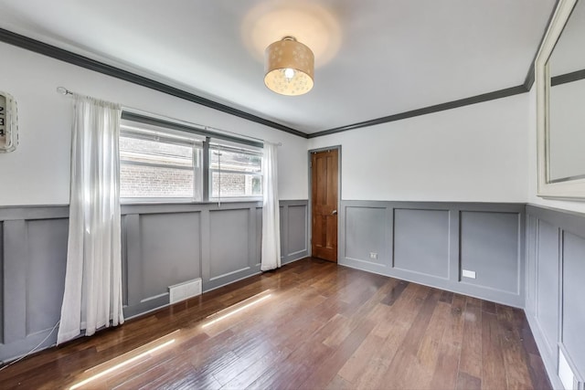 spare room featuring a decorative wall, a wainscoted wall, crown molding, and dark wood-style floors