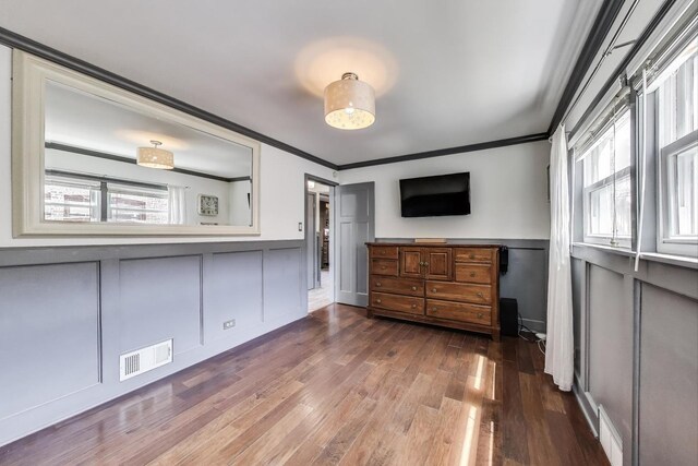 unfurnished bedroom with a decorative wall, ornamental molding, wainscoting, and dark wood finished floors