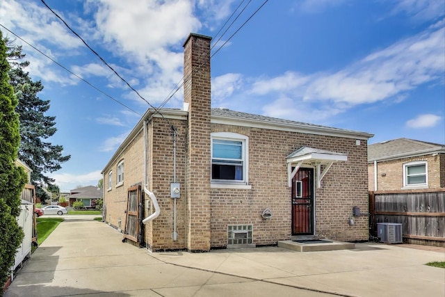 view of front of property with central air condition unit, brick siding, a chimney, and fence