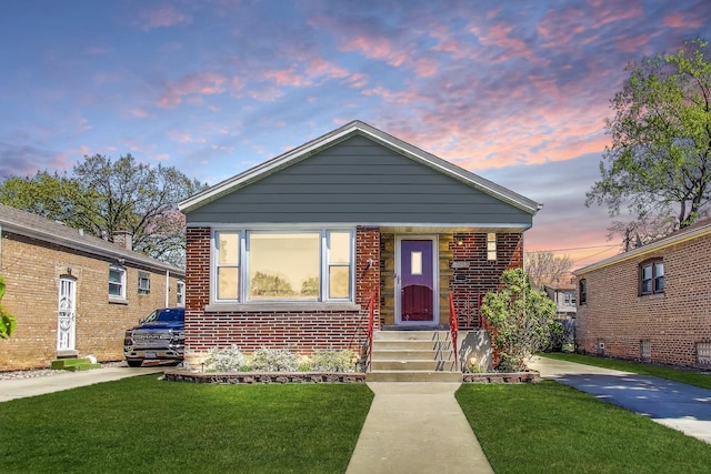 bungalow-style home with a yard, brick siding, and entry steps