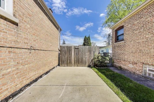 view of side of home featuring fence, brick siding, and a patio