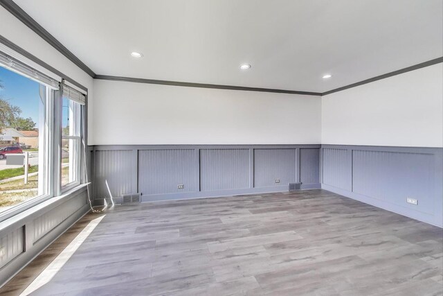 empty room with crown molding, a decorative wall, wainscoting, recessed lighting, and wood finished floors