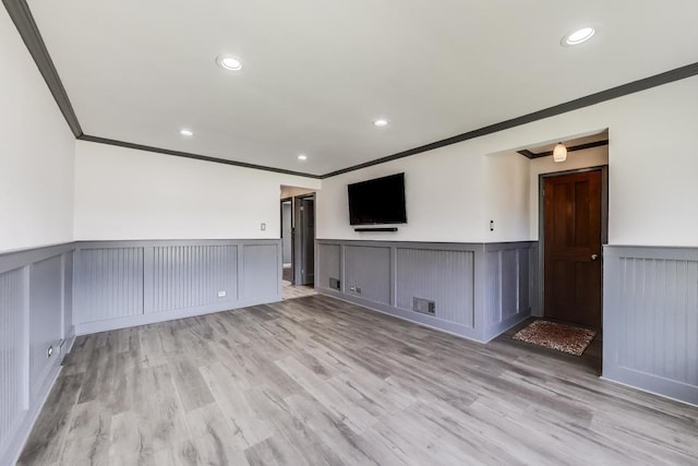 unfurnished living room with ornamental molding, wainscoting, light wood-type flooring, a decorative wall, and recessed lighting