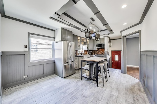kitchen with stainless steel appliances, wainscoting, ornamental molding, decorative backsplash, and gray cabinetry