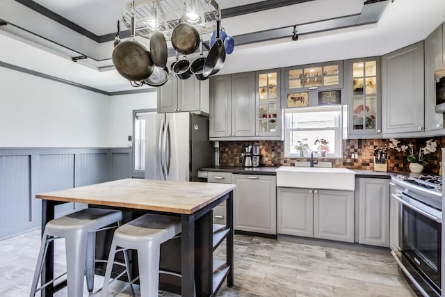 kitchen with appliances with stainless steel finishes, a sink, gray cabinets, ornamental molding, and backsplash