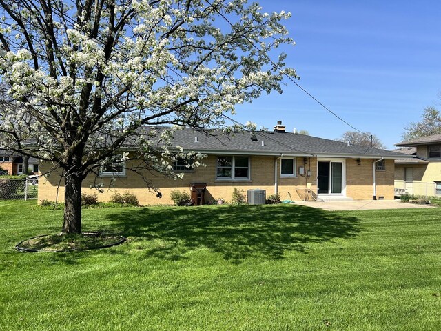 rear view of property with a lawn, brick siding, central AC unit, and a patio area