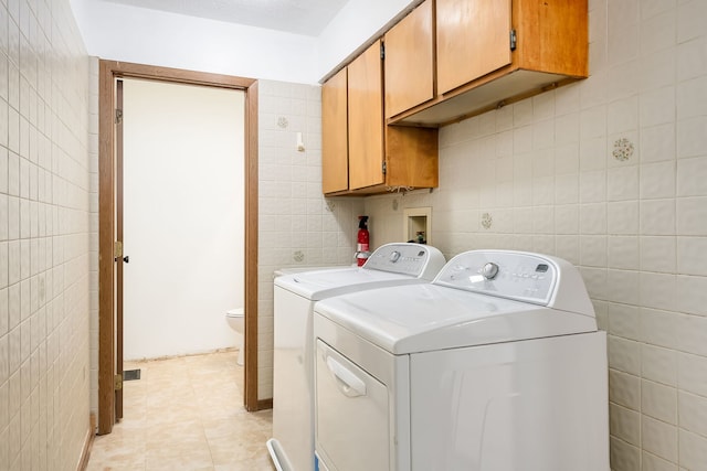 laundry room featuring independent washer and dryer, tile walls, light tile patterned floors, and cabinet space