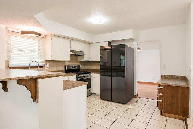 kitchen with white cabinets, appliances with stainless steel finishes, a textured ceiling, a peninsula, and under cabinet range hood