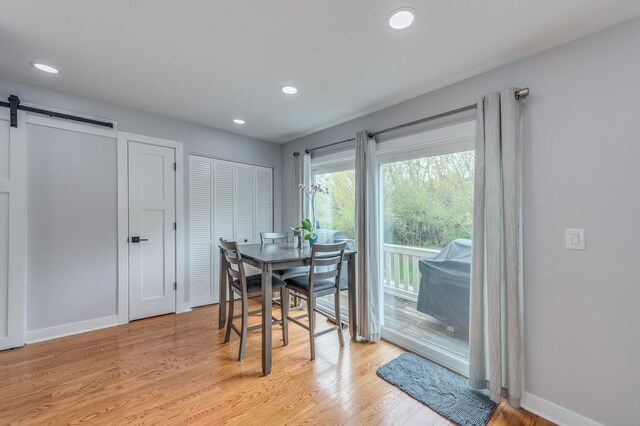 dining room with recessed lighting, a barn door, and light wood-type flooring