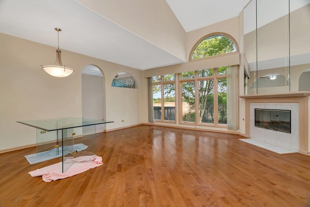 7017 Plymouth Ct, Tinley Park, IL 60477 - unfurnished living room featuring baseboards, wood finished floors, arched walkways, a tile fireplace, and a high ceiling