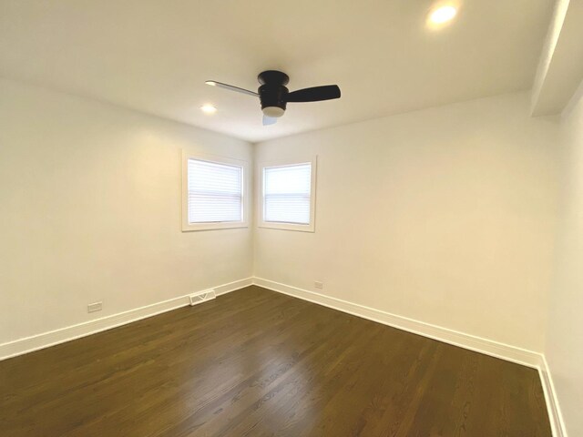 empty room with baseboards, a ceiling fan, dark wood finished floors, and visible vents