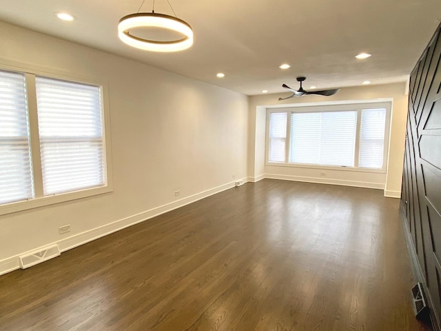 empty room featuring baseboards, ceiling fan, dark wood finished floors, and visible vents