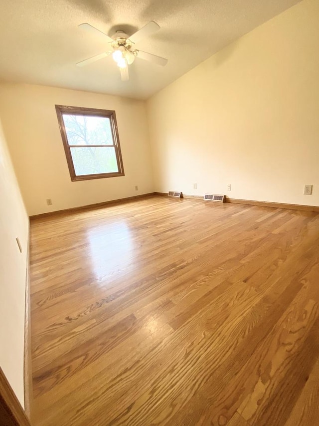 empty room with baseboards, ceiling fan, wood finished floors, and visible vents