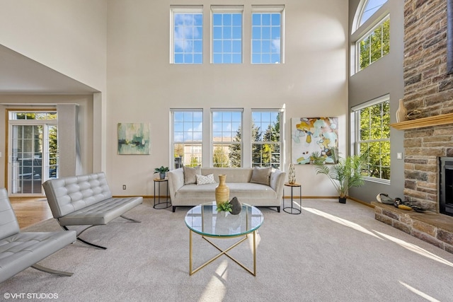 carpeted living area featuring a high ceiling, baseboards, and a stone fireplace