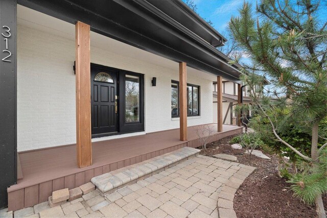 entrance to property with a porch and brick siding