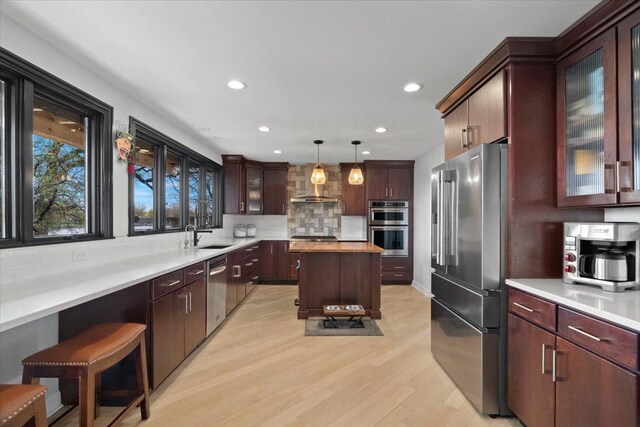kitchen with appliances with stainless steel finishes, wall chimney exhaust hood, recessed lighting, light wood-type flooring, and backsplash