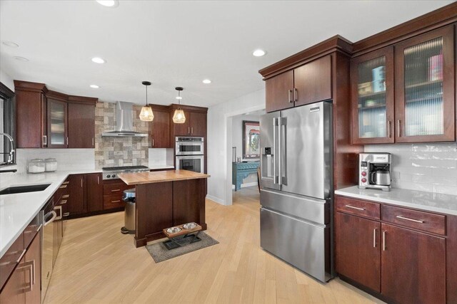 kitchen featuring a sink, decorative backsplash, appliances with stainless steel finishes, and wall chimney range hood
