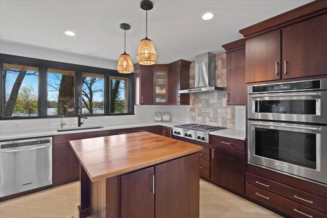 kitchen with appliances with stainless steel finishes, a sink, wood counters, wall chimney exhaust hood, and a kitchen island