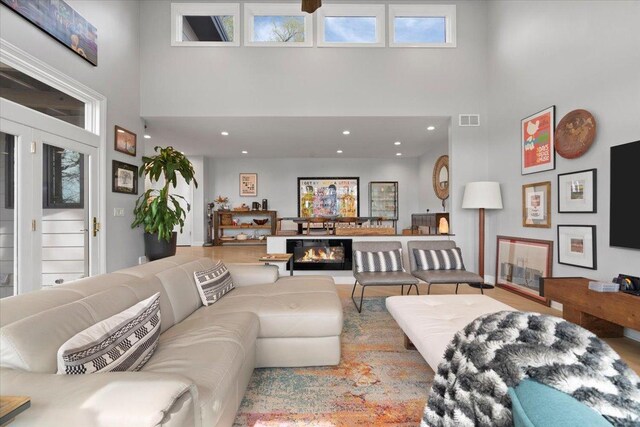 living area with visible vents, plenty of natural light, a high ceiling, and wood finished floors