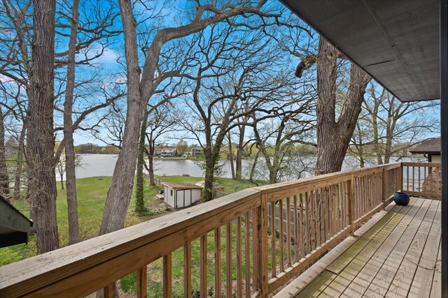 deck with an outdoor structure, a water view, a lawn, and a storage shed