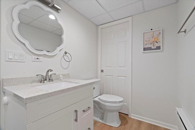 bathroom with vanity, toilet, wood finished floors, and a paneled ceiling