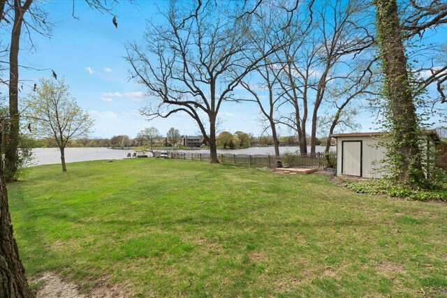 view of yard featuring an outdoor structure, a water view, fence, and a storage shed