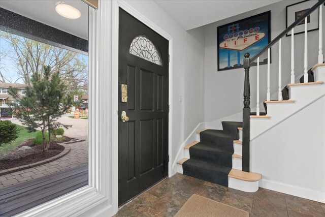 foyer entrance with baseboards, stone finish floor, and stairway