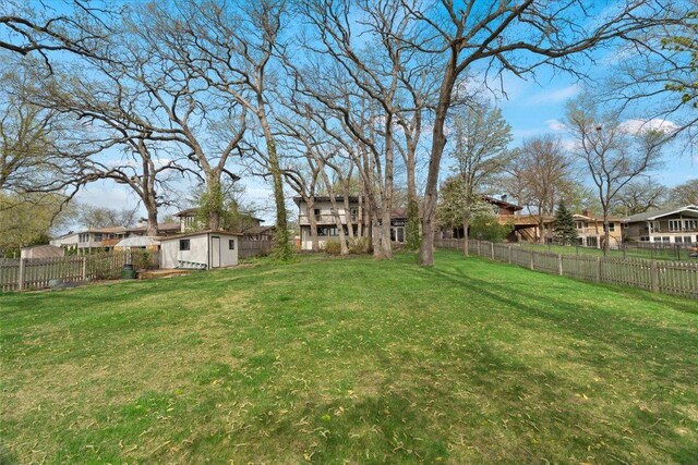 view of yard featuring a fenced backyard, a shed, an outbuilding, and a residential view