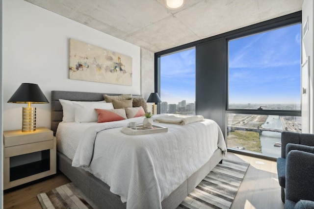 bedroom with a wall of windows, a view of city, and wood finished floors