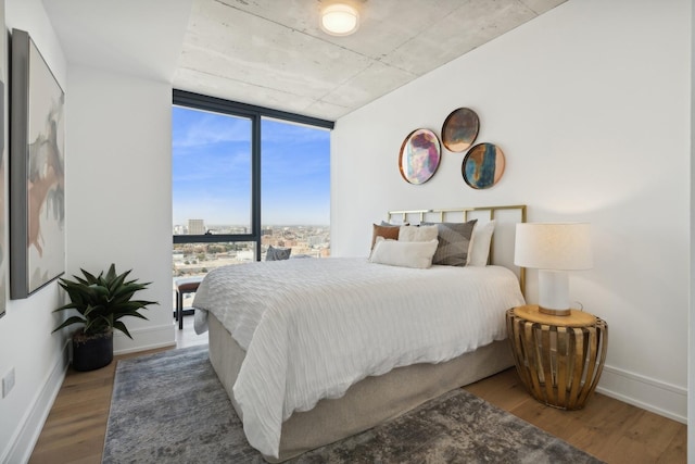 bedroom with expansive windows, a city view, baseboards, and wood finished floors