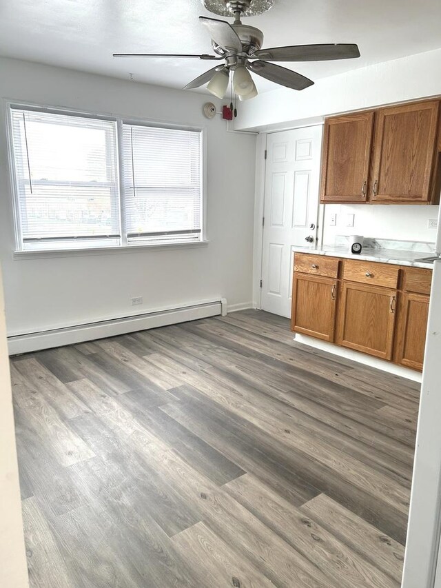 kitchen featuring a ceiling fan, brown cabinets, wood finished floors, a baseboard heating unit, and a wealth of natural light