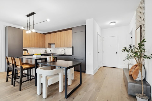 kitchen with decorative backsplash, modern cabinets, a sink, light wood finished floors, and dark countertops