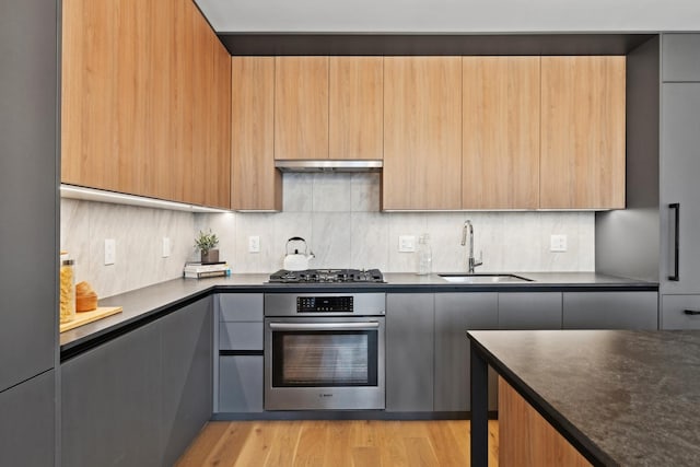 kitchen featuring stainless steel appliances, a sink, modern cabinets, dark countertops, and extractor fan