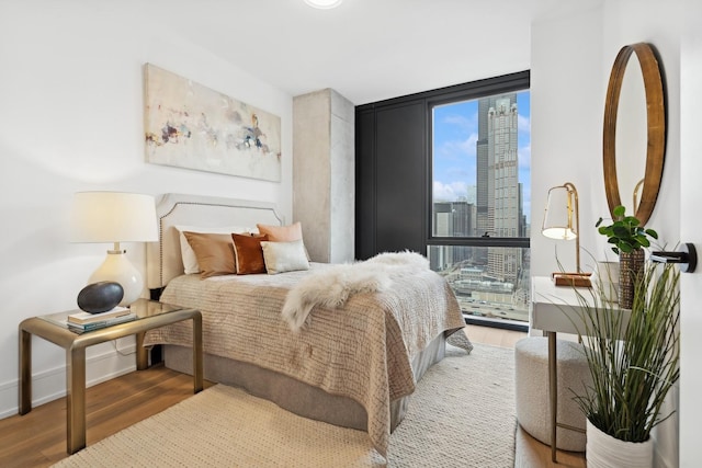 bedroom featuring wood finished floors, a wall of windows, multiple windows, a skyline view, and baseboards
