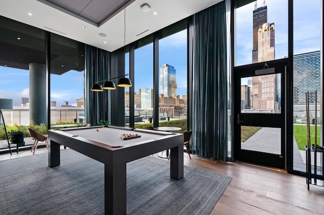 game room with floor to ceiling windows, a skyline view, healthy amount of natural light, and wood finished floors