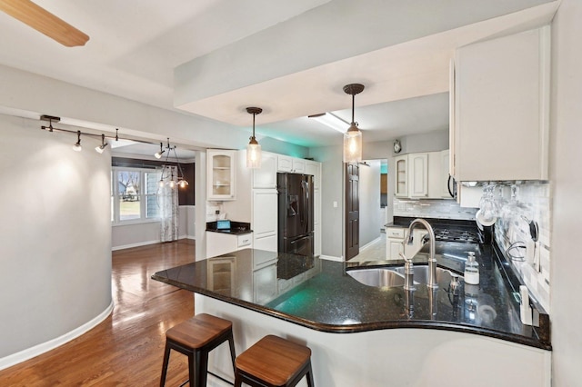 kitchen with black fridge with ice dispenser, a peninsula, baseboards, white cabinetry, and a sink