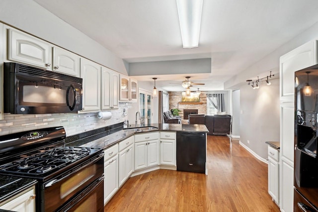 kitchen with ceiling fan, a sink, a stone fireplace, a peninsula, and black appliances