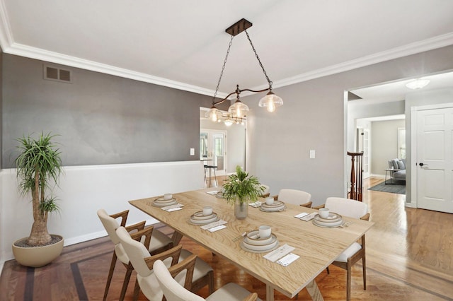 dining area with visible vents, wood finished floors, baseboards, a notable chandelier, and ornamental molding