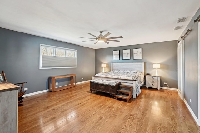 bedroom featuring visible vents, a barn door, baseboards, and wood finished floors