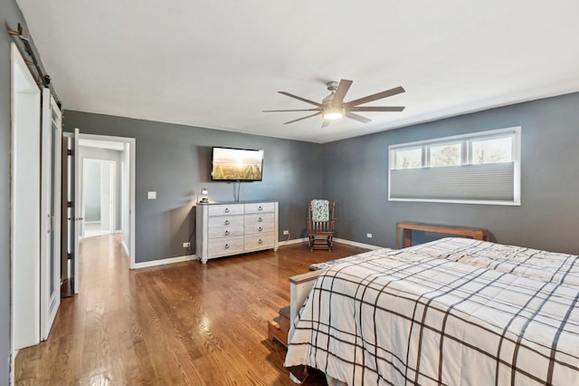 bedroom featuring a ceiling fan, baseboards, a barn door, and wood finished floors