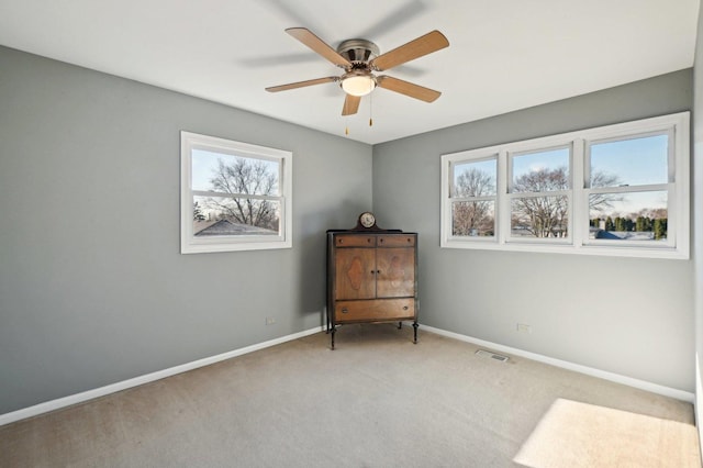 interior space featuring baseboards, multiple windows, a ceiling fan, and visible vents