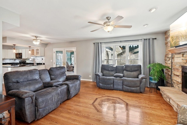 living room featuring light wood-style floors, baseboards, ceiling fan, and a fireplace