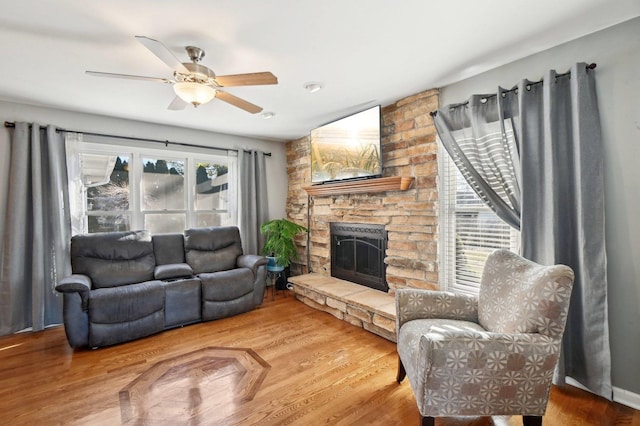 living area with a stone fireplace, a ceiling fan, and wood finished floors